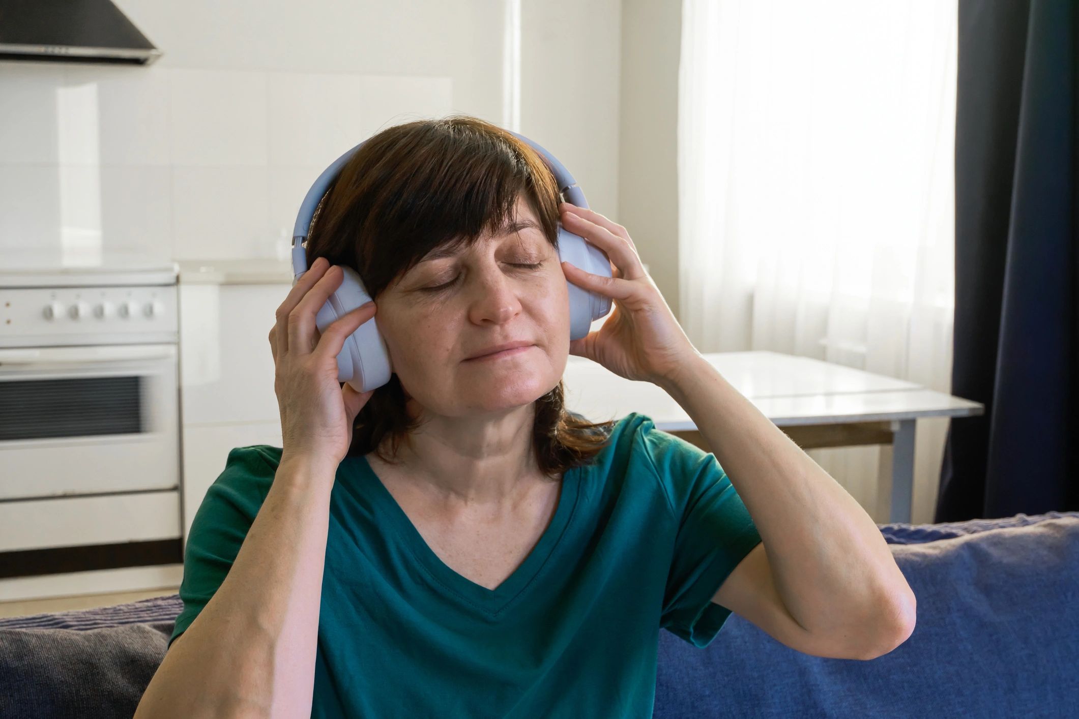 Mature woman listening to music on wireless headphones, calm and comfortable
